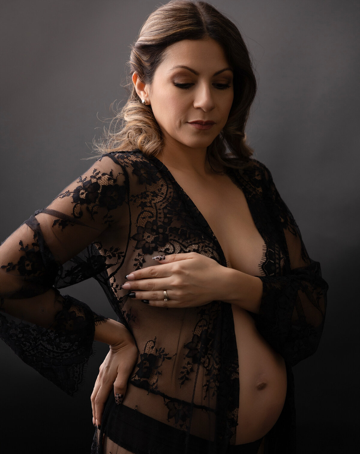 Pregnant mom wearing a black sheer robe and showing her bare belly and looking down toward her belly.
