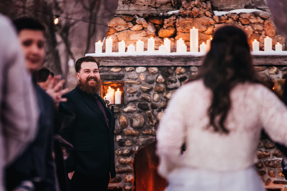 Groom smiling at bride as she walks down the aisle in winter Whitney's Inn wedding in Jackson NH by Lisa Smith Photography