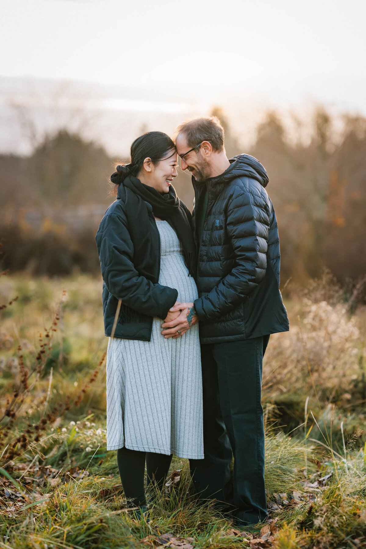 Pregnant couple sharing an intimate moment, putting their foreheads together and smiling with love and connection.