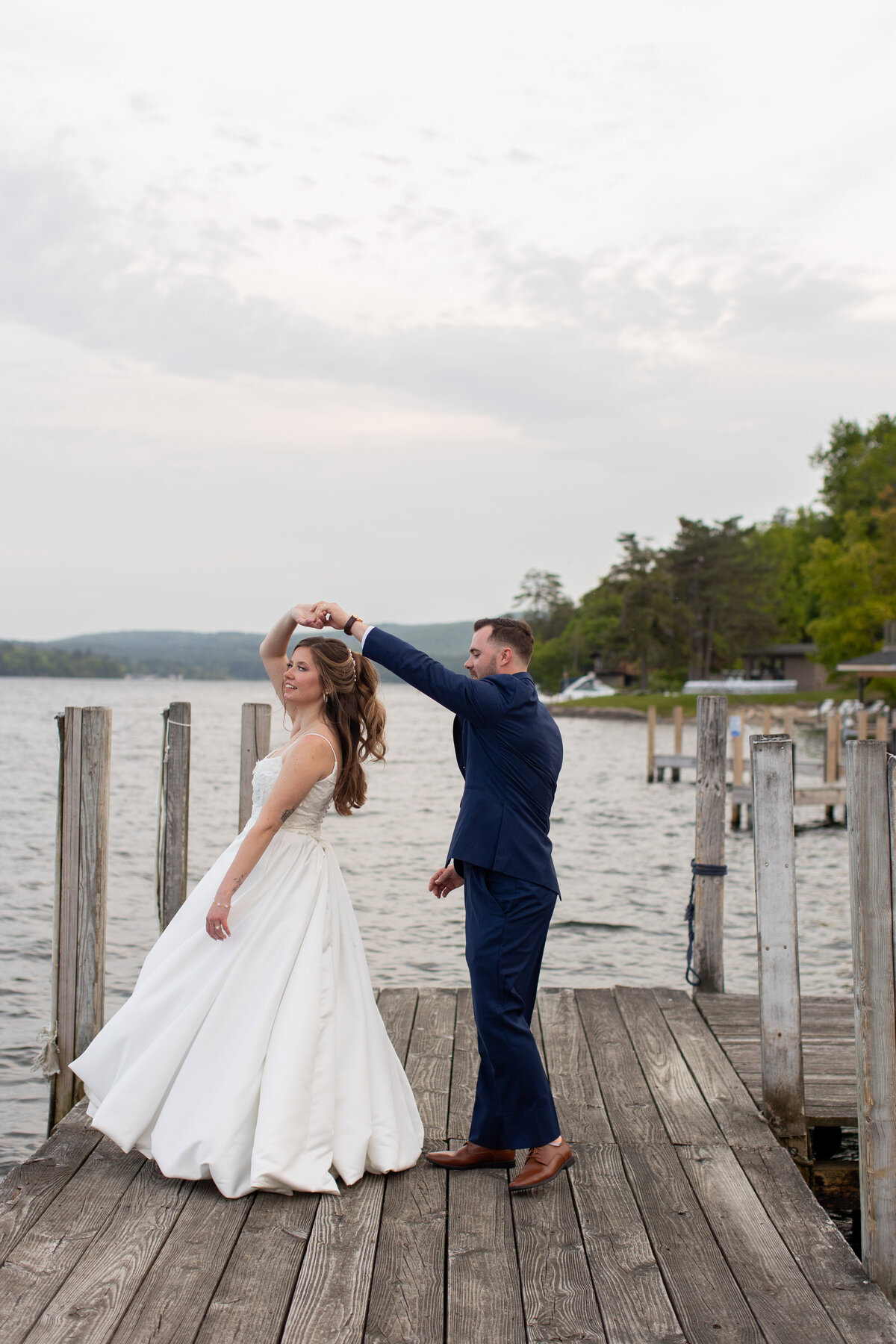 Groom twirls bride on the dock of a lake
