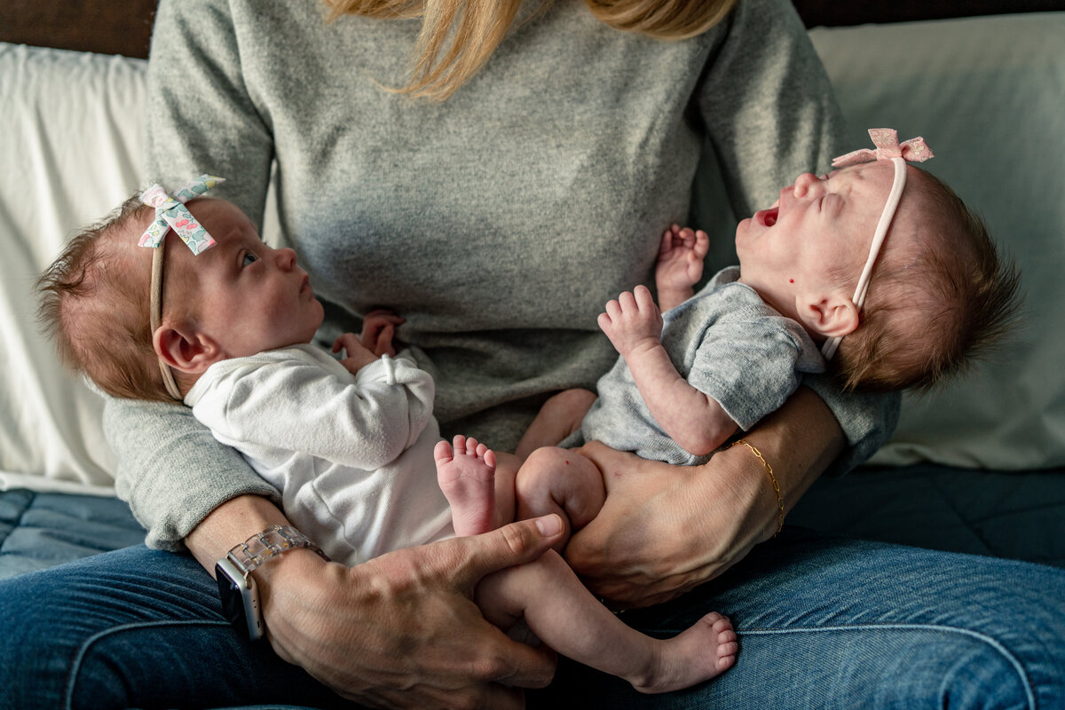 Twin baby girls in mom's arms during in home newborn photo session