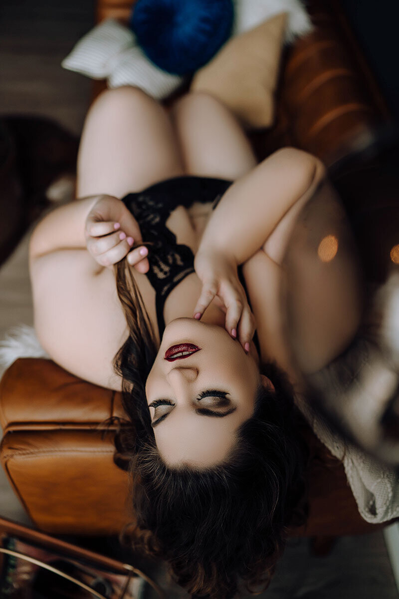 Curvy woman in dark red lipstick posing over orange leather couch