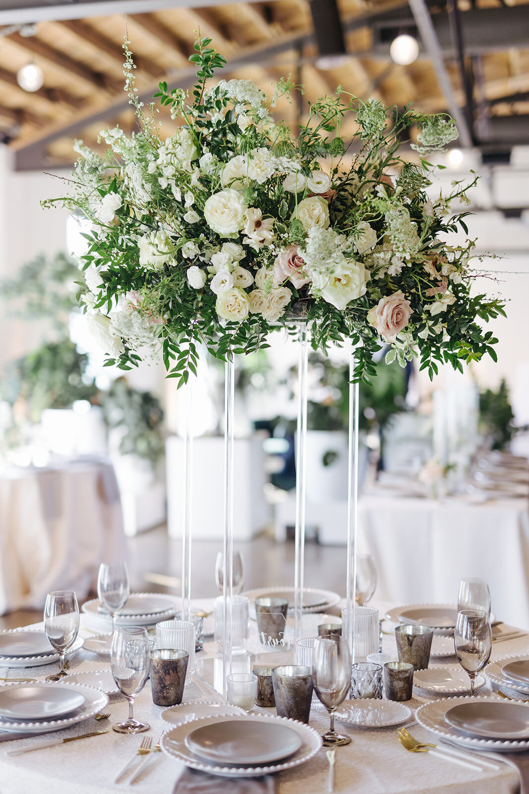 Elevated lucite stands with lush floral centerpieces of white garden roses, ranunculus, delphinium, lisianthus, Queen Anne’s lace and natural, untamed greenery. Floral hues of white, cream, and blush. Designed by Rosemary and Finch in Nashville, TN.