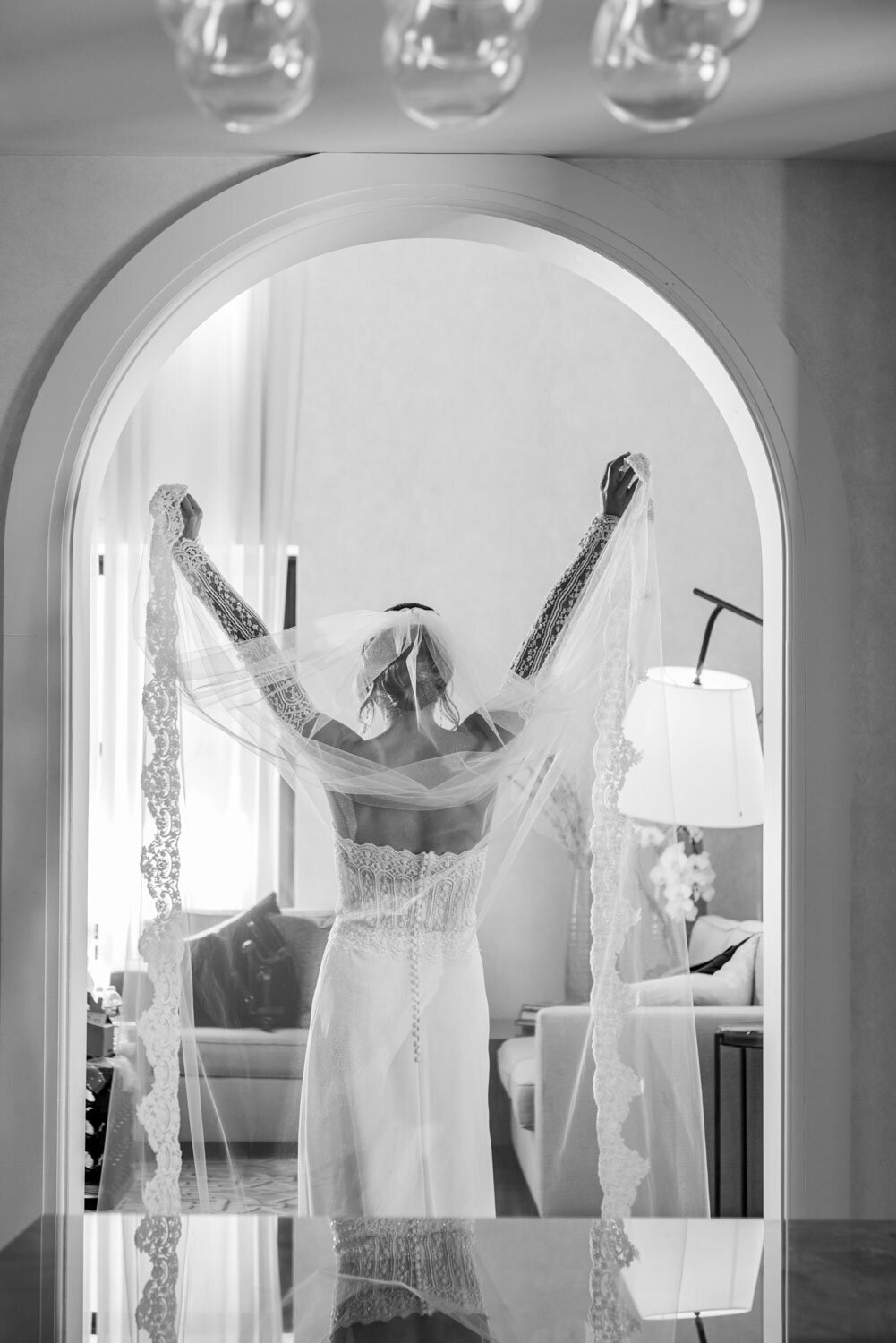 A woman in a wedding dress and veil is standing in a room with her arms outstretched.