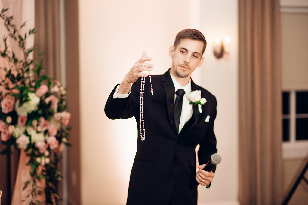 Wedding Photograph Of Groom In Black Suit Holding Out a Necklace Los Angeles