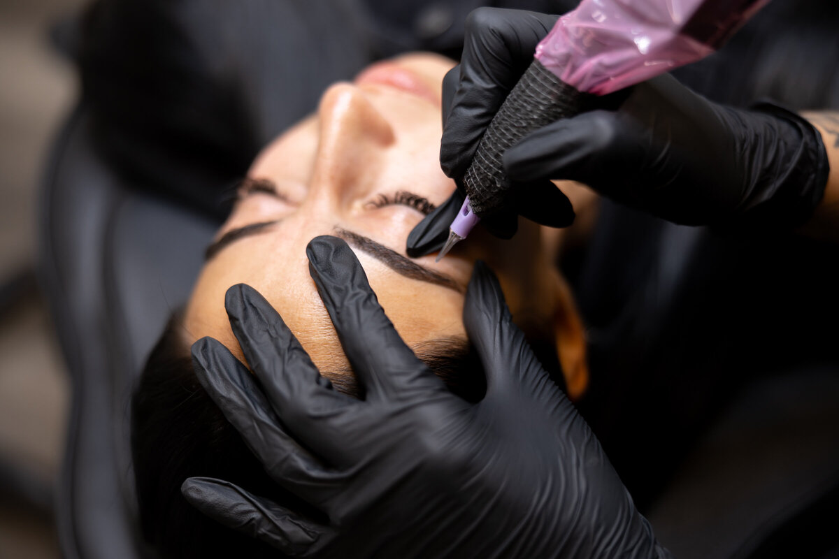 Tattoo artist with tattoos smiling while working on a client in a salon chair. Photograph by Yucaipa branding photographer Kaitlyn Dawn Photography.