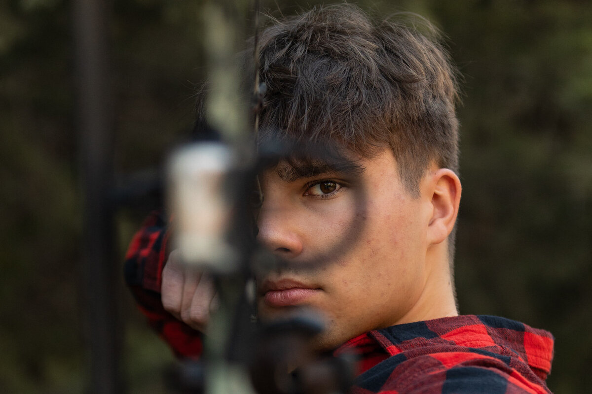 A senior guy looking through a bows eye while getting a picture taken in Lawrence, KS