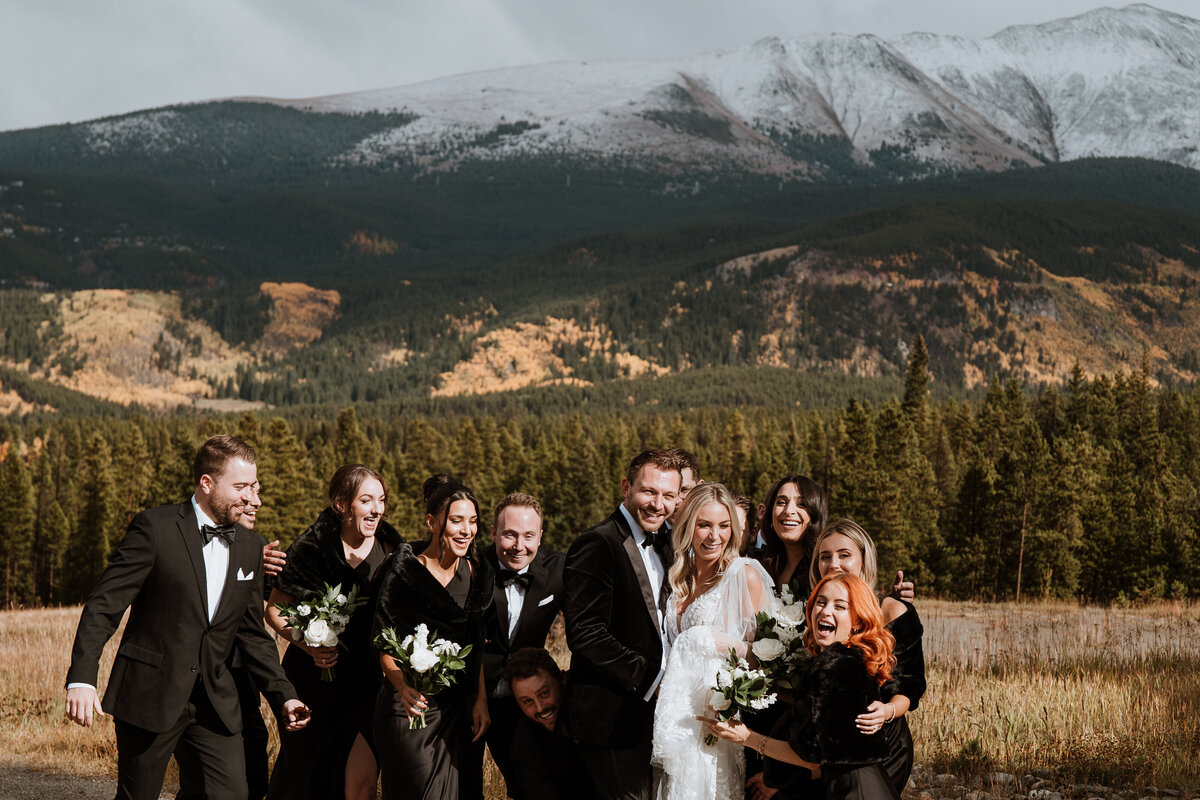 Wedding party poses with joyful energy in front of snow-capped Breckenridge mountains.