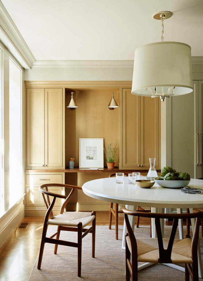 A timeless dining area with custom oak cabinets, a white round table, and walnut Wishbone chairs, all swathed in natural daylight. Designed by Sarah Scales.