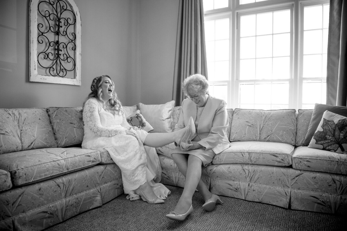 Bride laughing indoors while mom puts on shoe