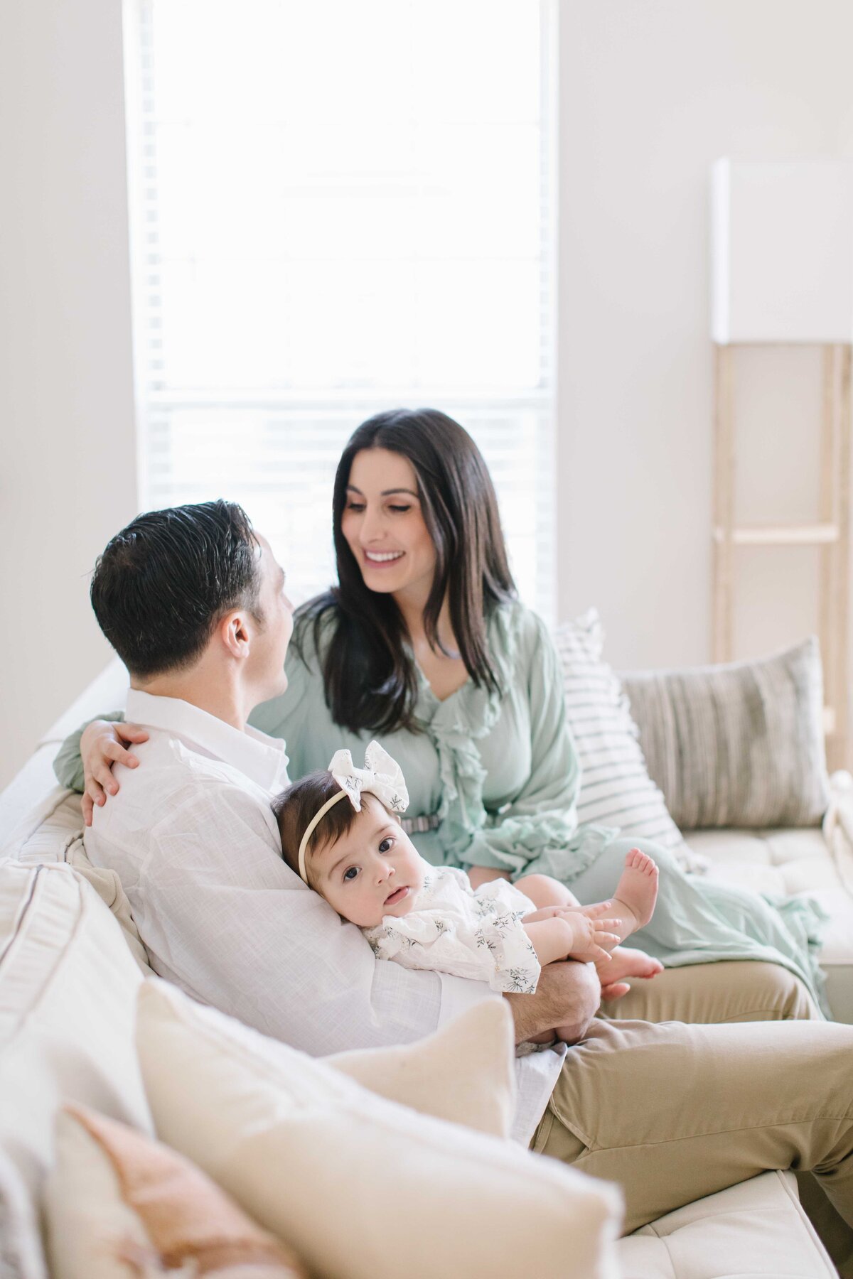 family of three lounging on couch and baby looking at photographer during in-home session