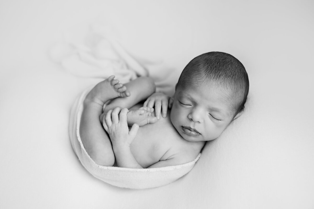 Newborn sleeping curled up on his back on a white background.