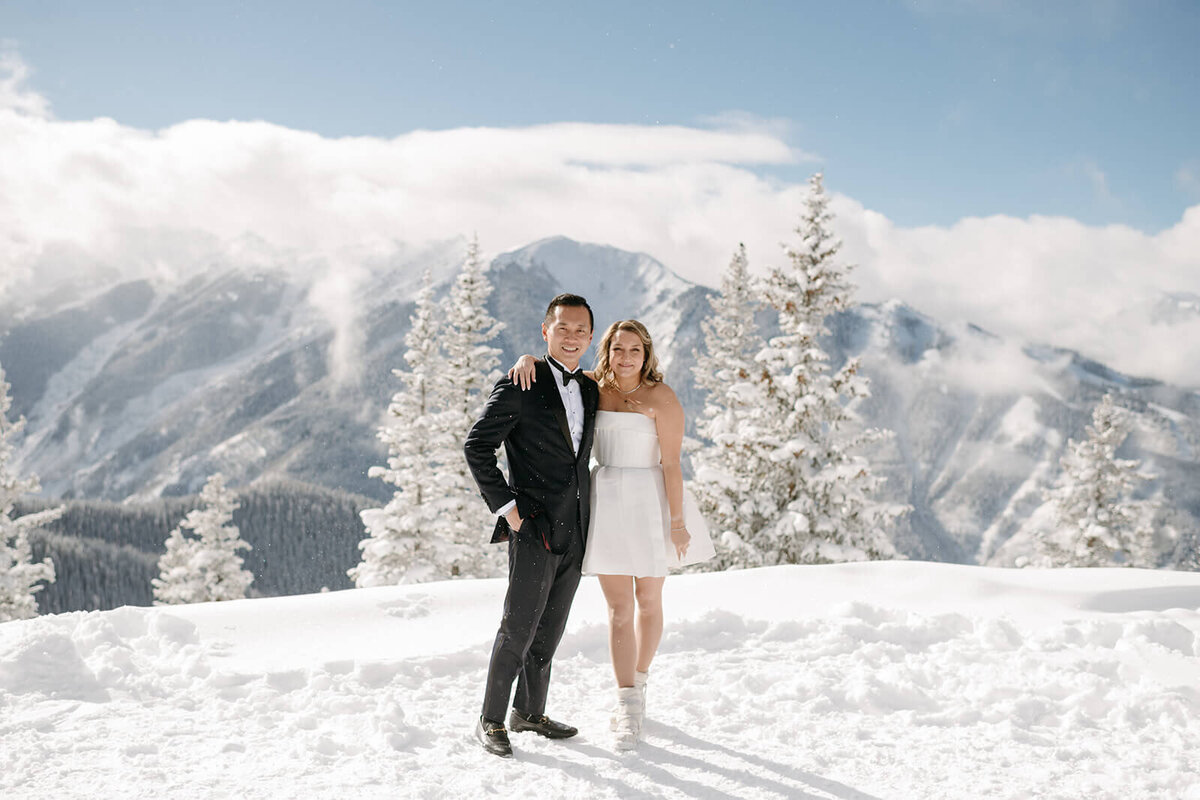 Bride and groom posing on a mountaintop at St. Regis Aspen, surrounded by breathtaking views of snow-capped peaks and blue skies.