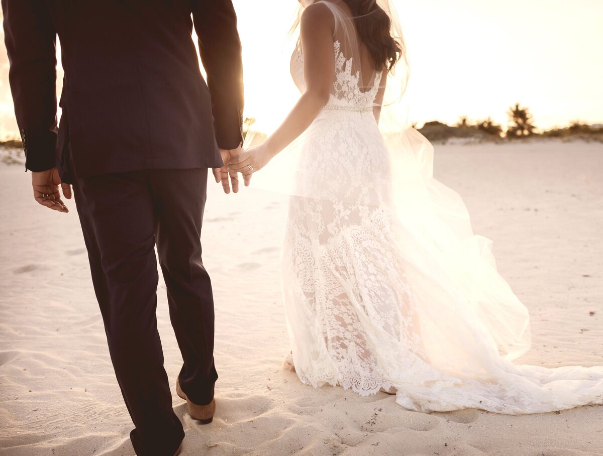 Close up of hands and feet of bride and groom walking away on beach in Cancun