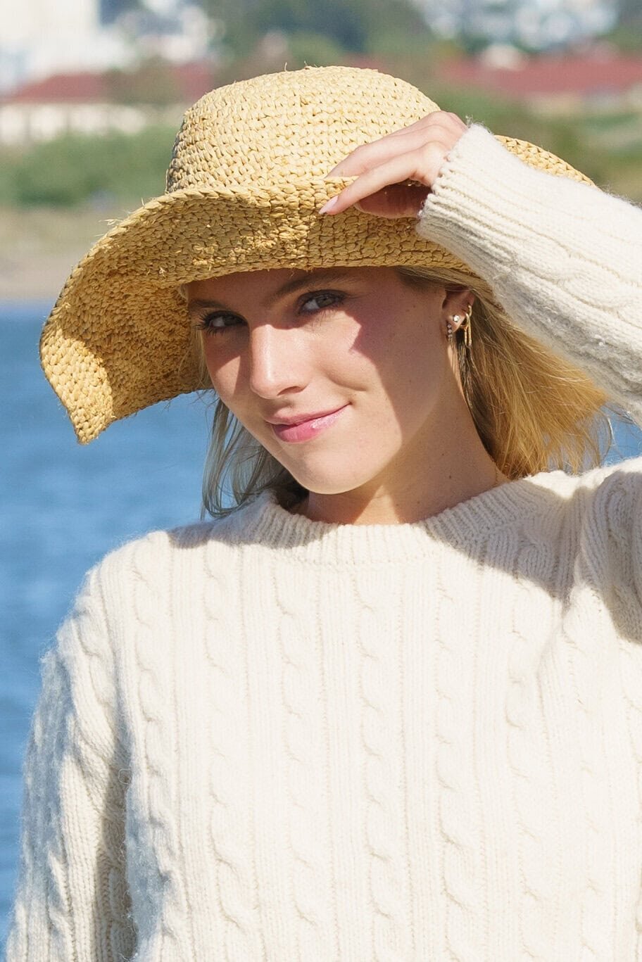 Young woman smiling while wearing a light sweater and a straw hat at the beach
