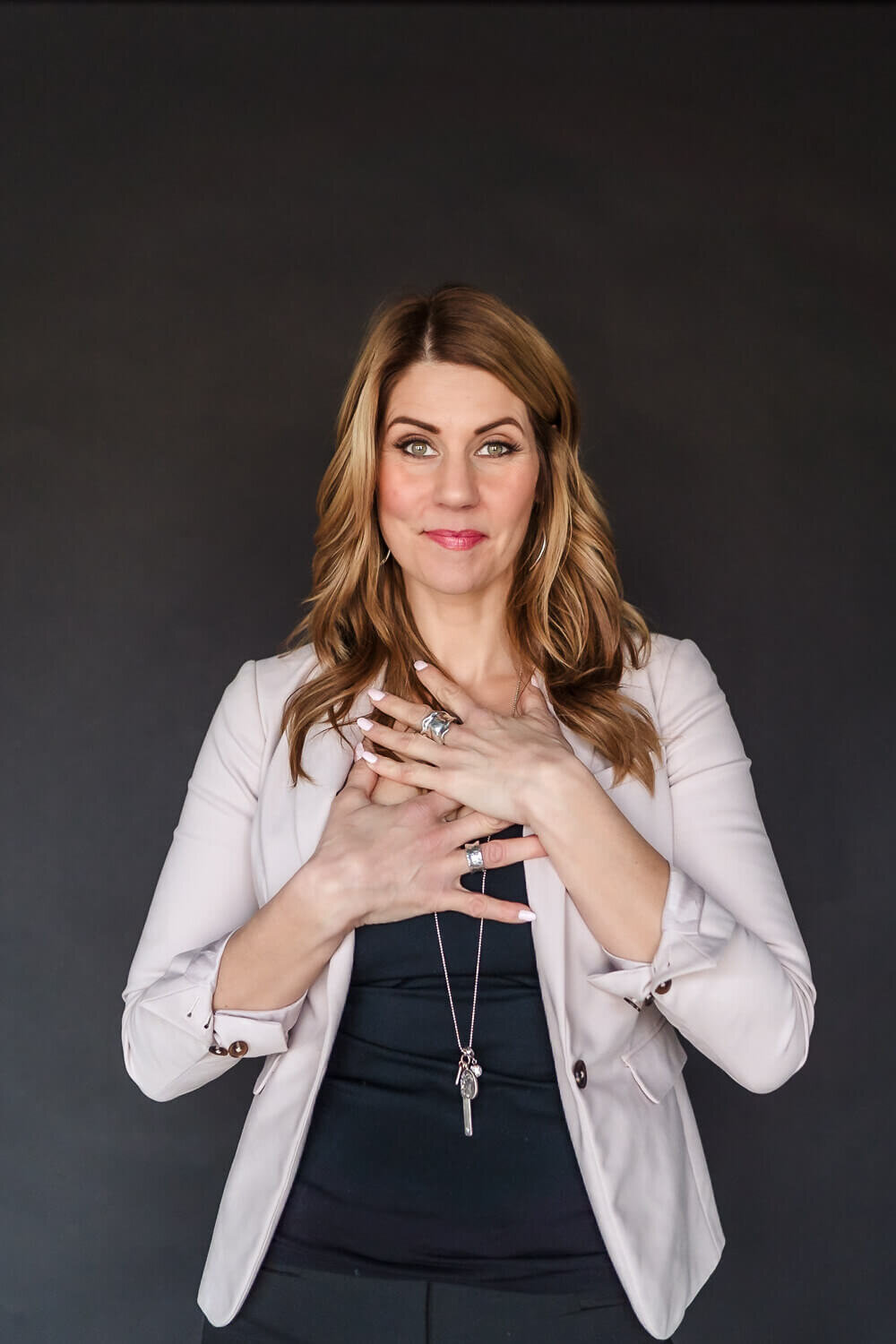 Smiling woman with hands on heart wearing pink blazer during brand photography shoot