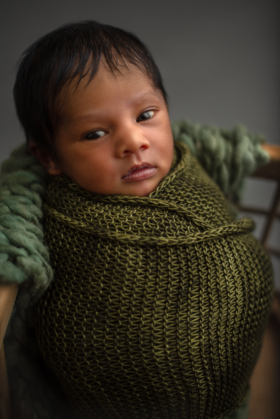 baby wrapped in green blanket and looking at camera by st louis newborn photographer