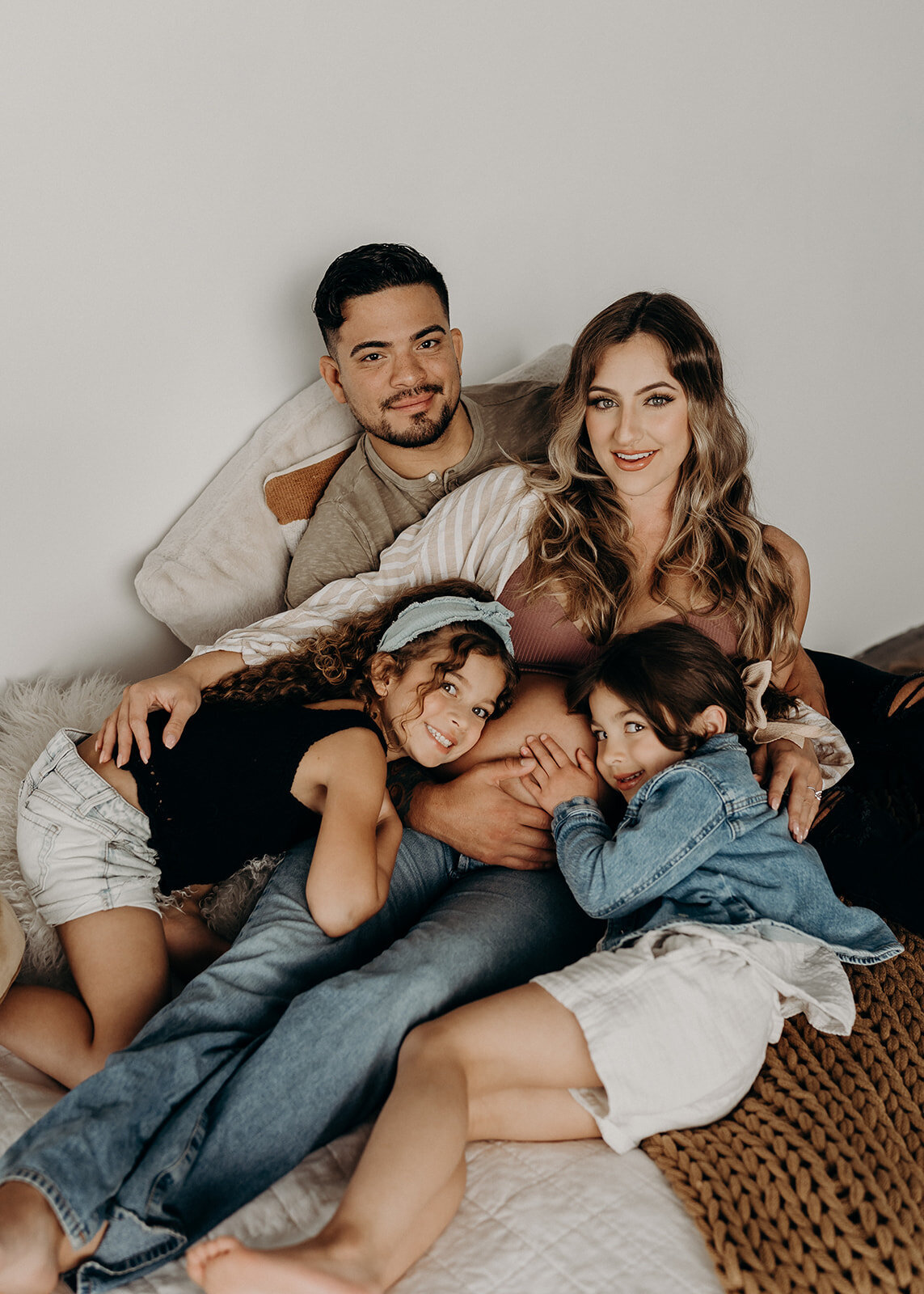 Family of four poses on a bed smiling at the camera