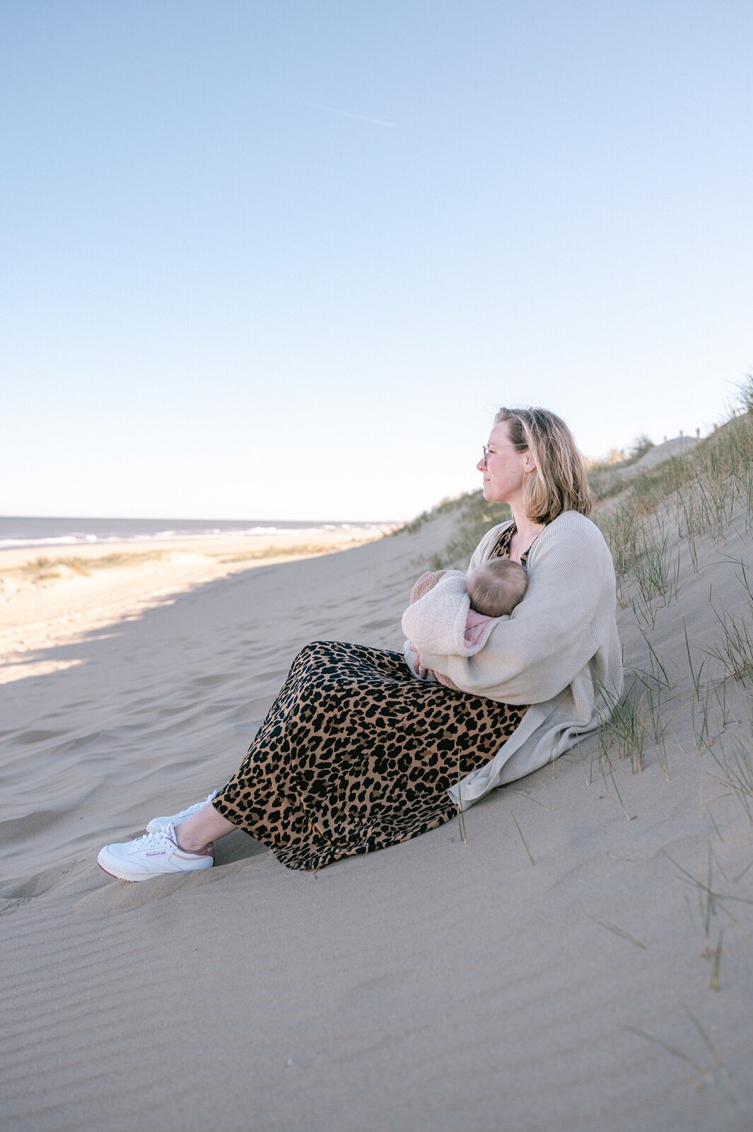 Moeder geeft borstvoeding op  het strand terwijl ze naar de zee kijkt