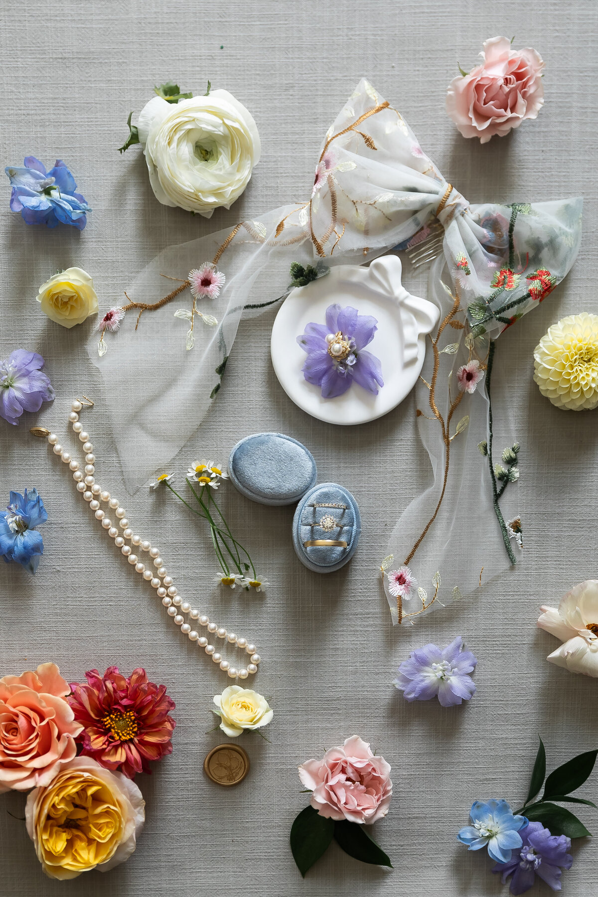 Wedding Photographers in RI | Kelsey Sheehan Photography Timeless Rhode Island Weddings | A romantic flat lay featuring a sheer floral scarf, pearl necklace, flowers, and blue ring box on a soft gray background. Elegant and tranquil tone.