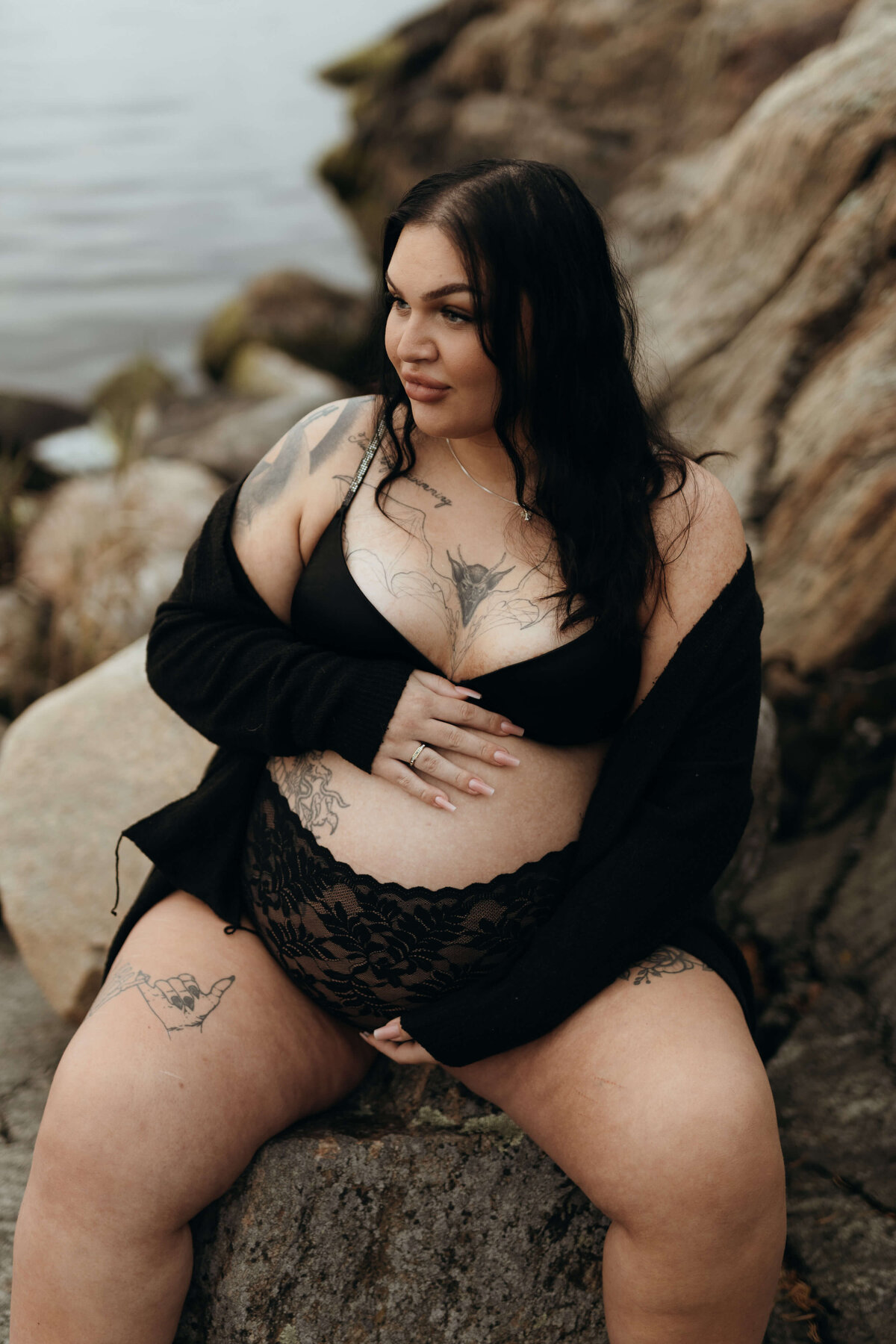 En gravid kvinna sittandes på en sten iklädd svarta underkläder under en gravidfotografering i Stockholm