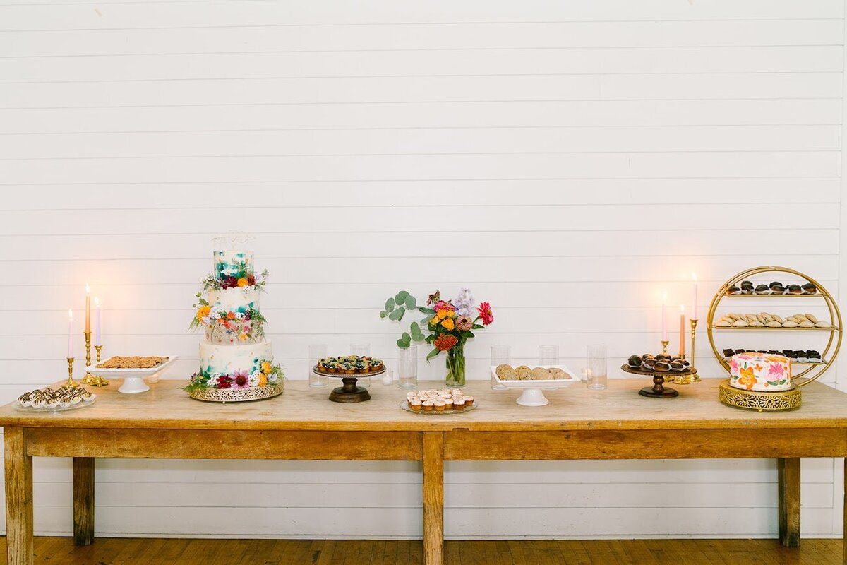 A further shot of a wooden cake filled with stands of different desserts, and a three tier colorful cake with flowers.