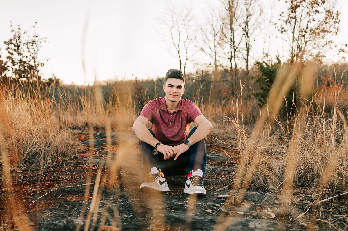 teenage boy sitting in field at sunset during Branson senior photography session