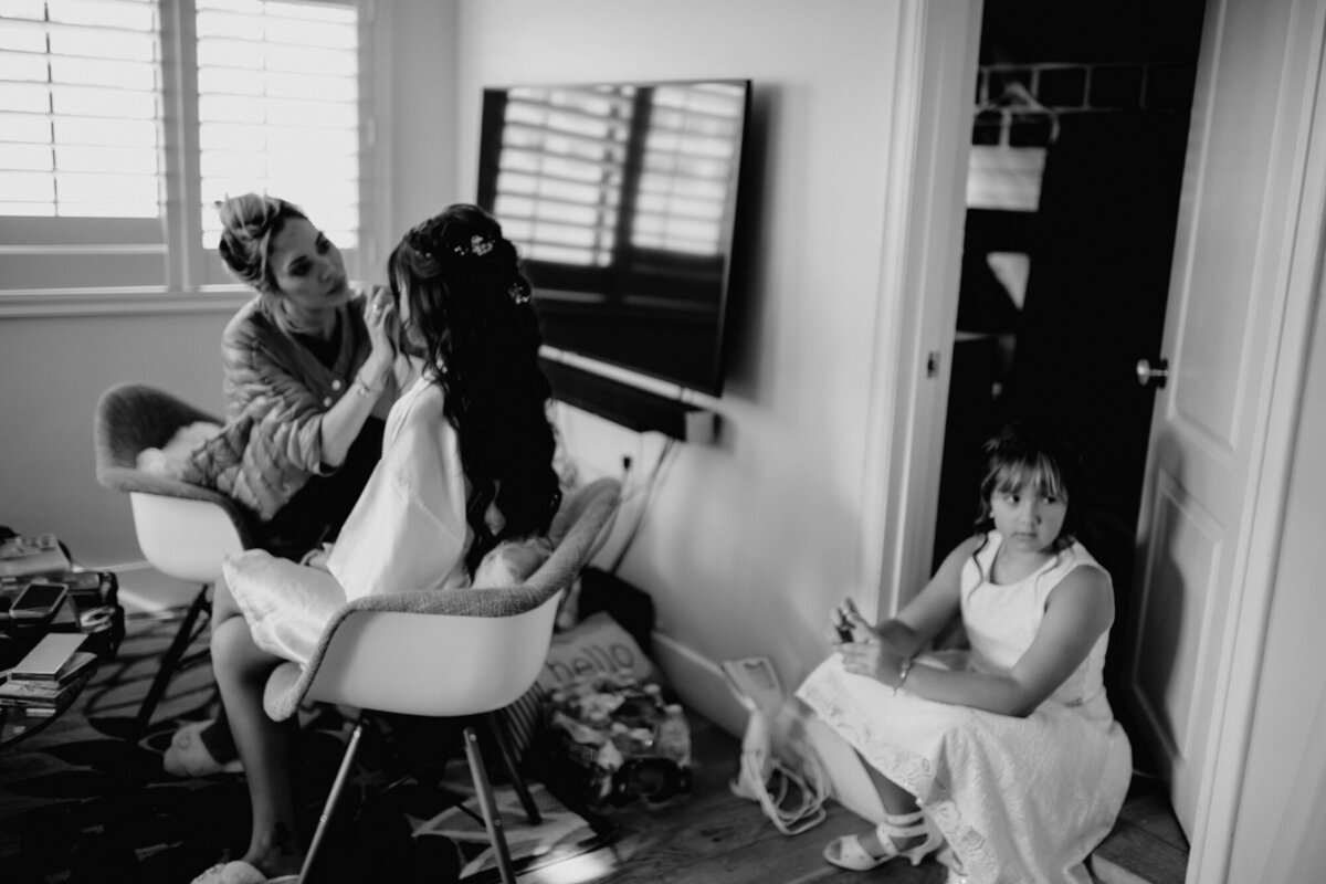 Black and white photo of Bride getting her makeup done by the Makeup artist with some of the other bridal party.