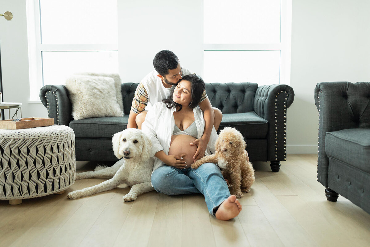 pregnant couple cudding at home on the floor with their dogs in nova