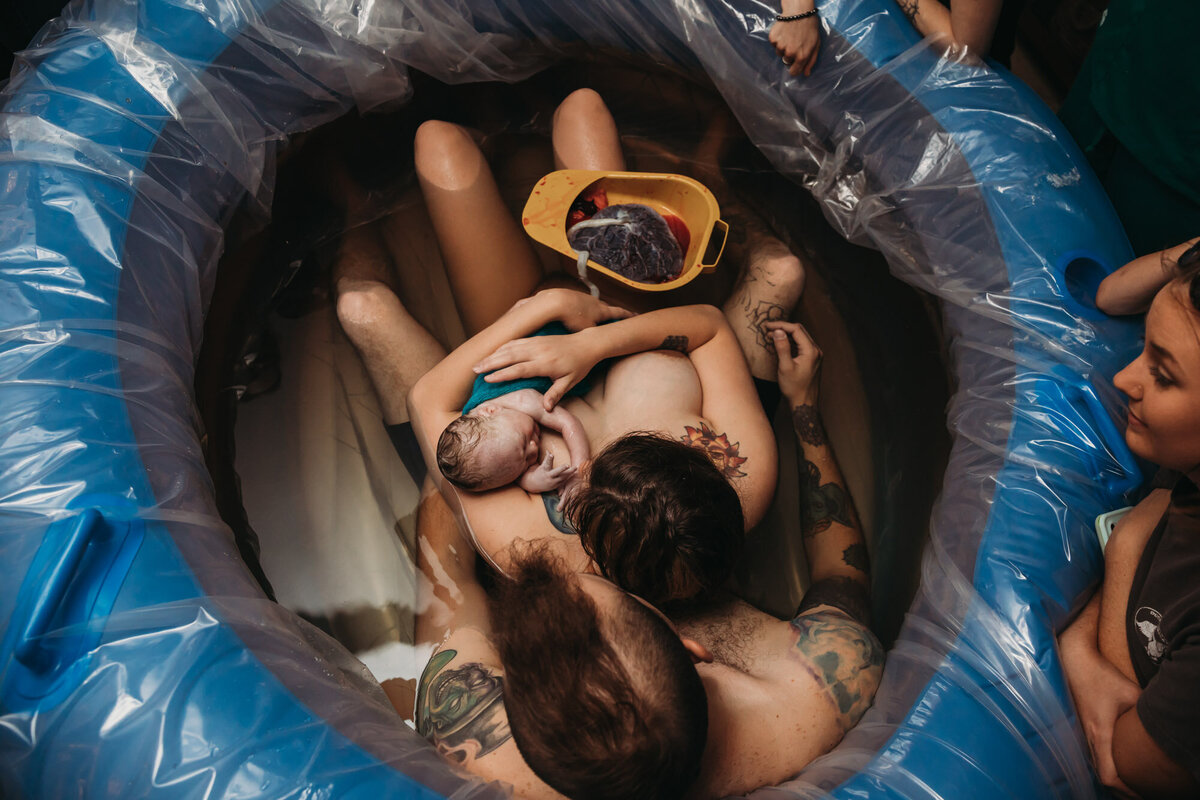 woman and man holding newborn in birth pool