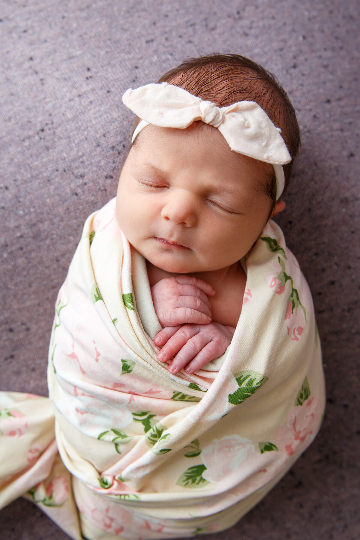 Picture of a newborn baby girl wrapped in a floral blanket with a bow on her head