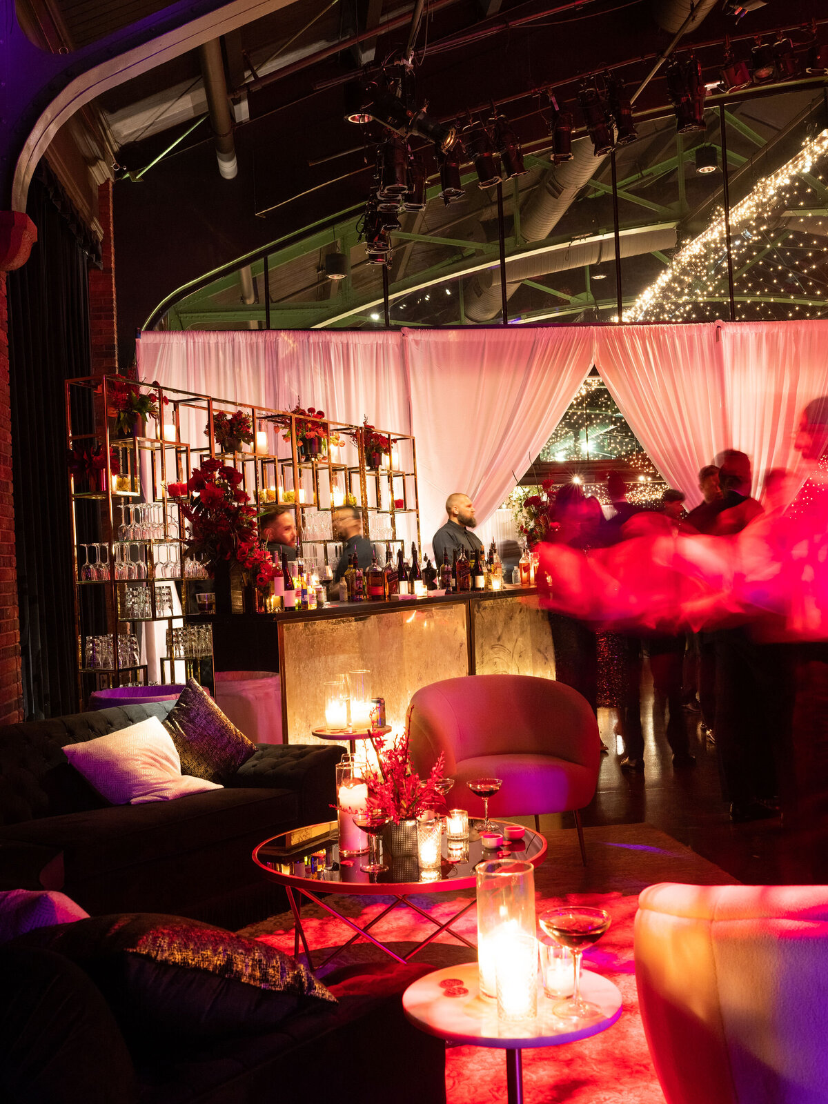 A stylish lounge area with plush seating, elegant floral arrangements, and a sophisticated bar setup with guests enjoying cocktails.