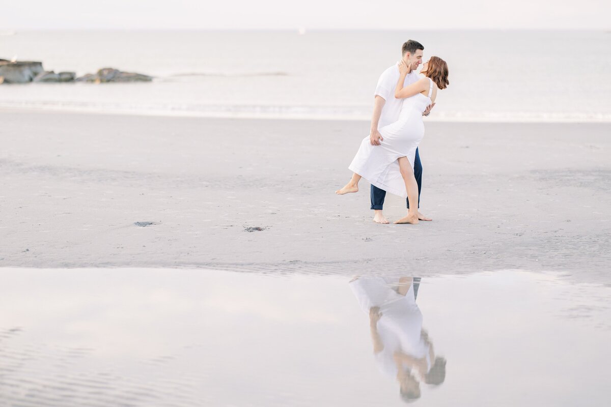 A man dipping a woman while dancing on Wingaersheek Beach during their engagement photography session.