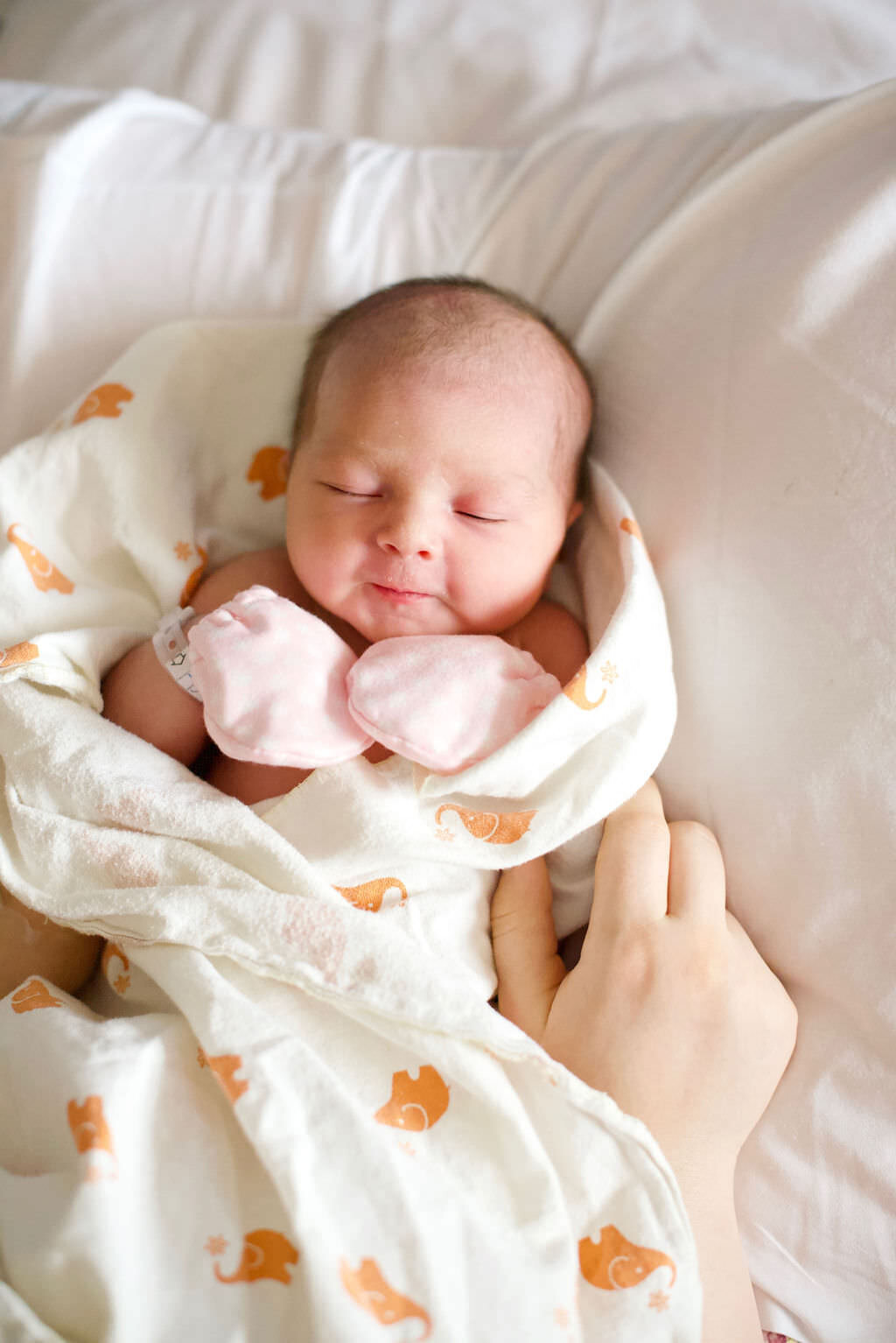 A newborn with pink gloves on sleeping.