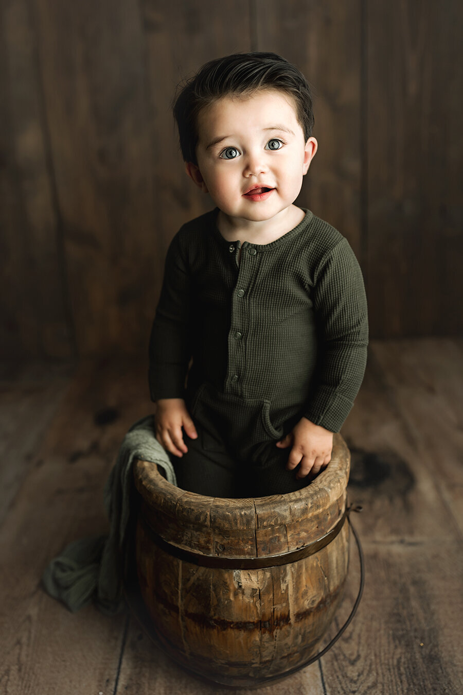 Cute baby boy sitting in a bucket with a funny expression on his face