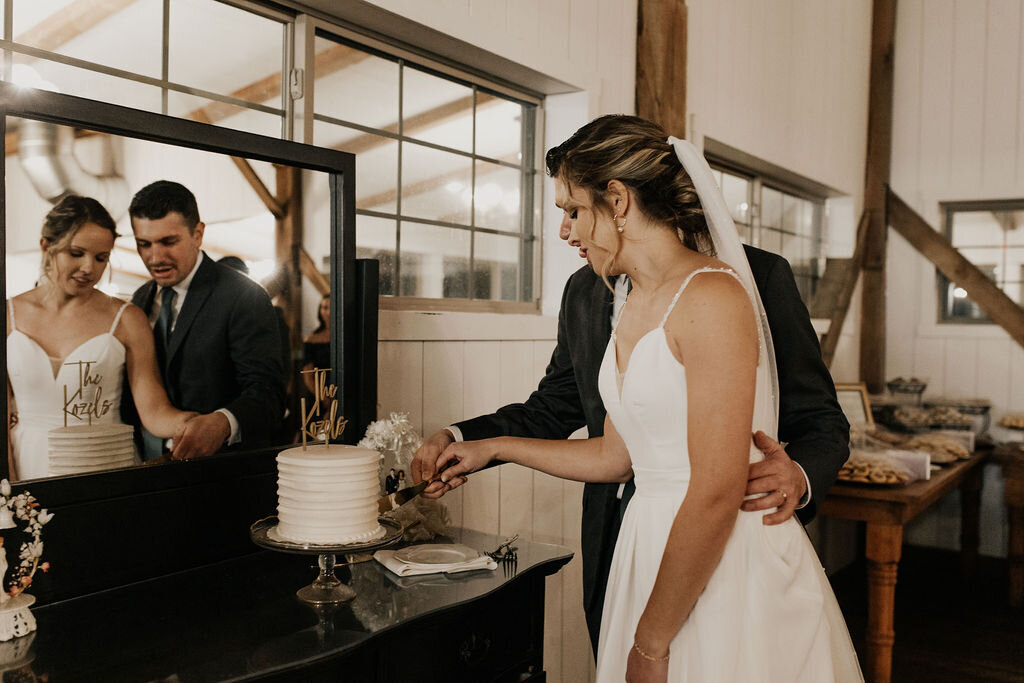 bride and groom cutting their wedding cake on a vintage dresser at Willowbrook wedding venue