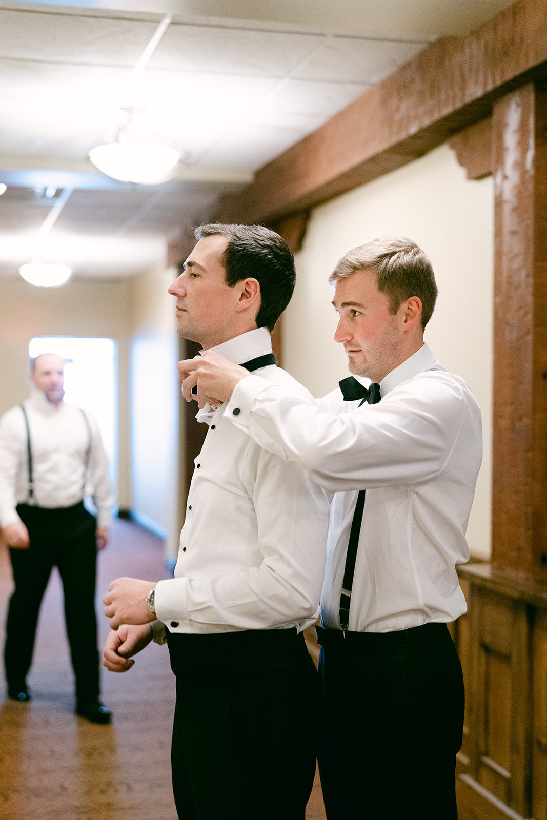 Bestman helping groom tie his tie shot by Philadelphia wedding photographer.