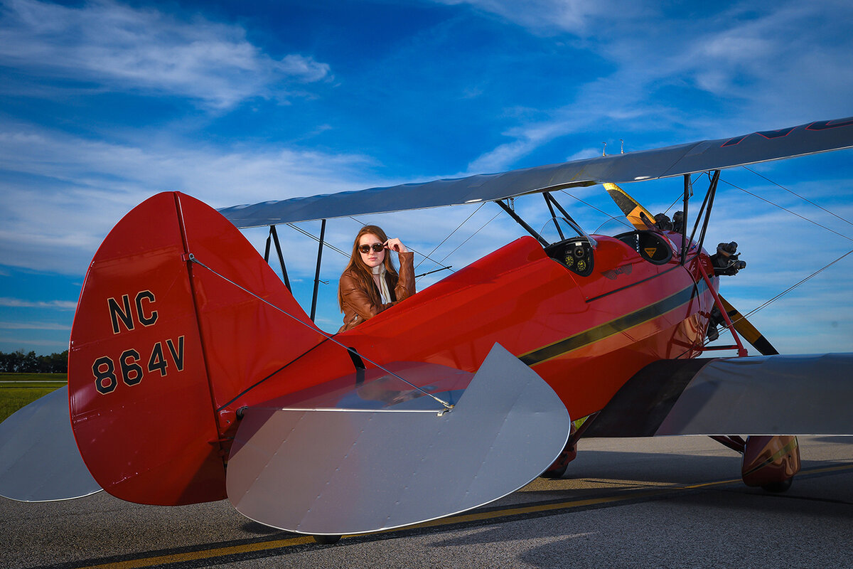 Teenage girl poses for senior portrait with red airplane