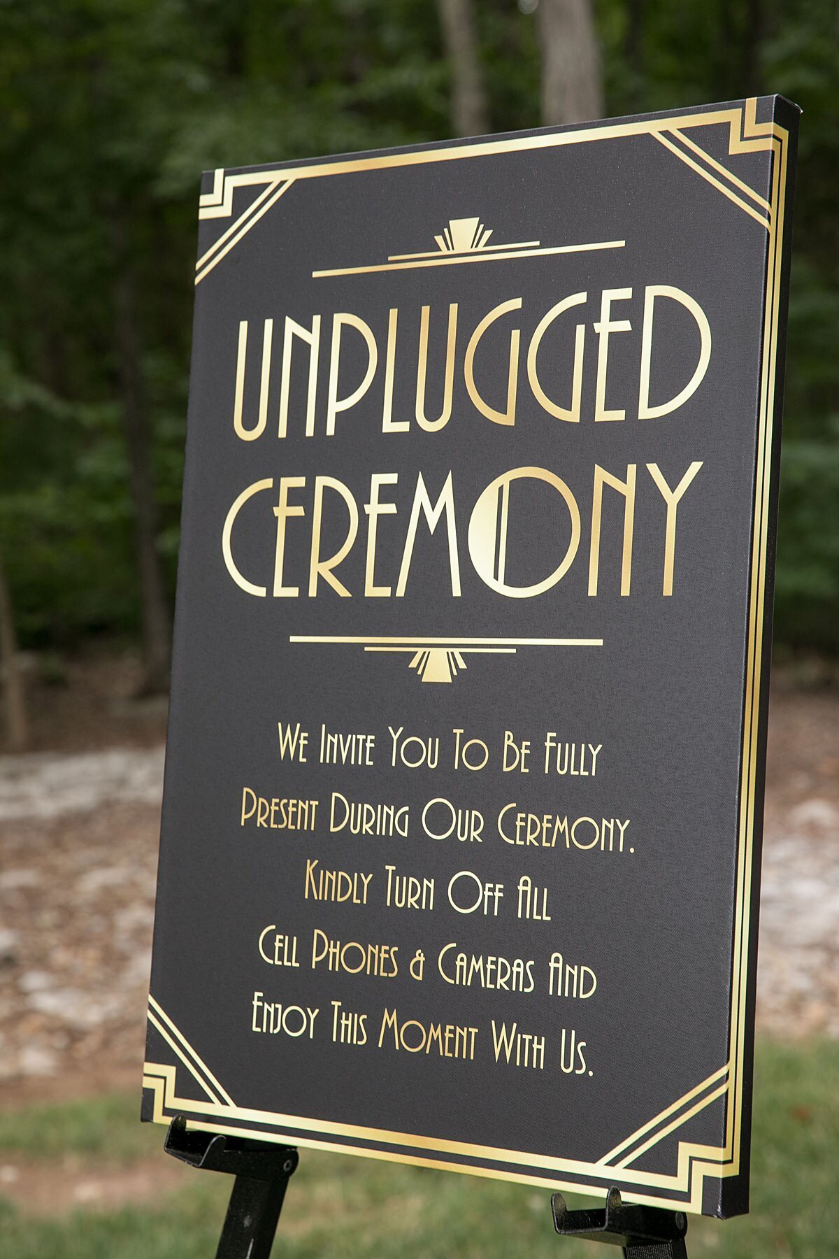 1920s art decor unplugged wedding ceremony sign in grey and gold  sitting on a black easel at Saddle Woods Farm.