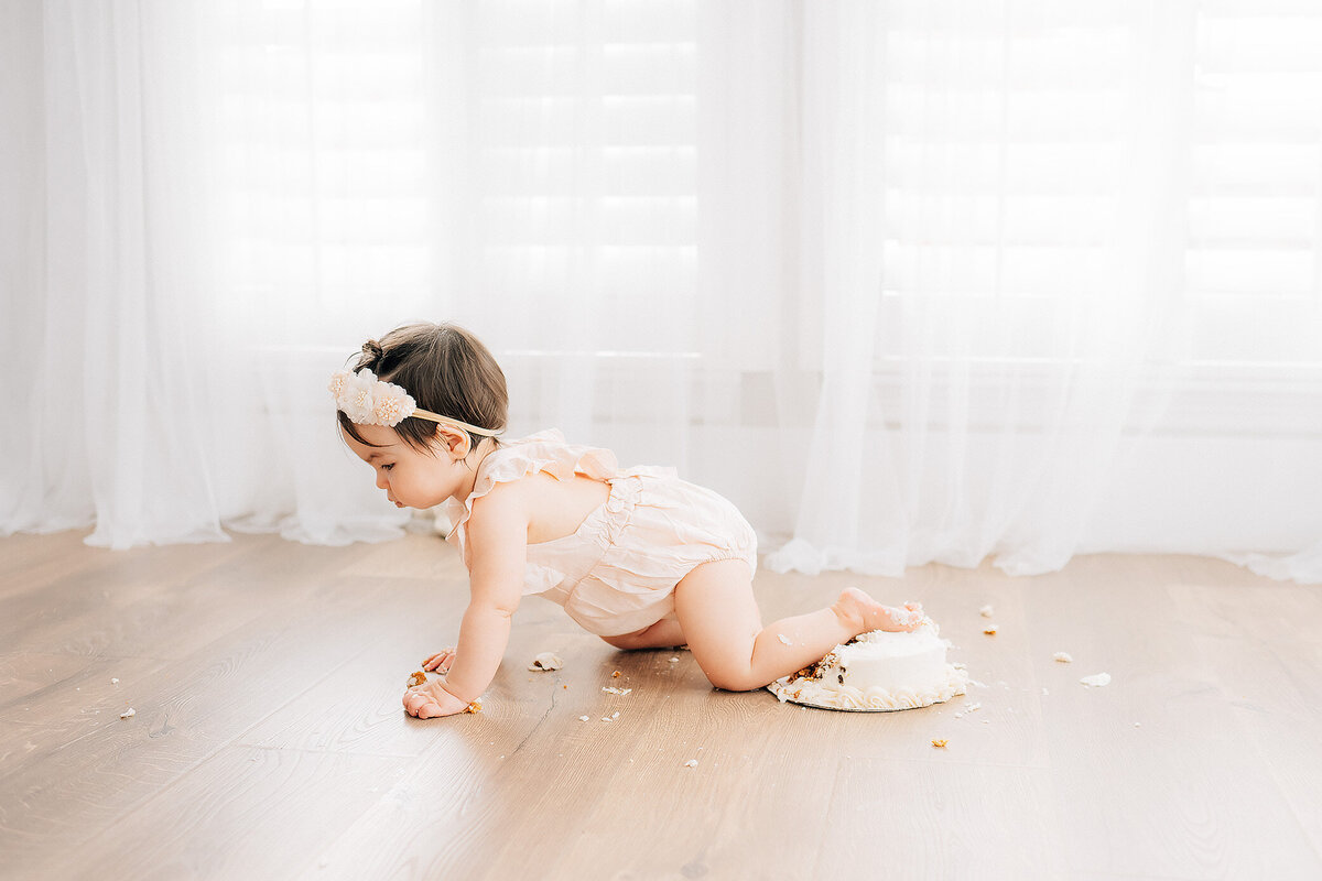 One year old milestone baby at photographer studio crawling over her birthday cake