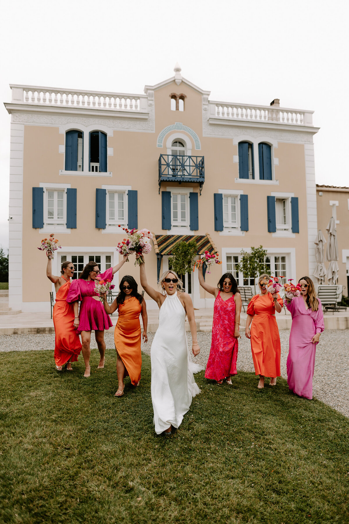 A bride leads her bridesmaids who are wearing pink and orange dress at a wedding in France