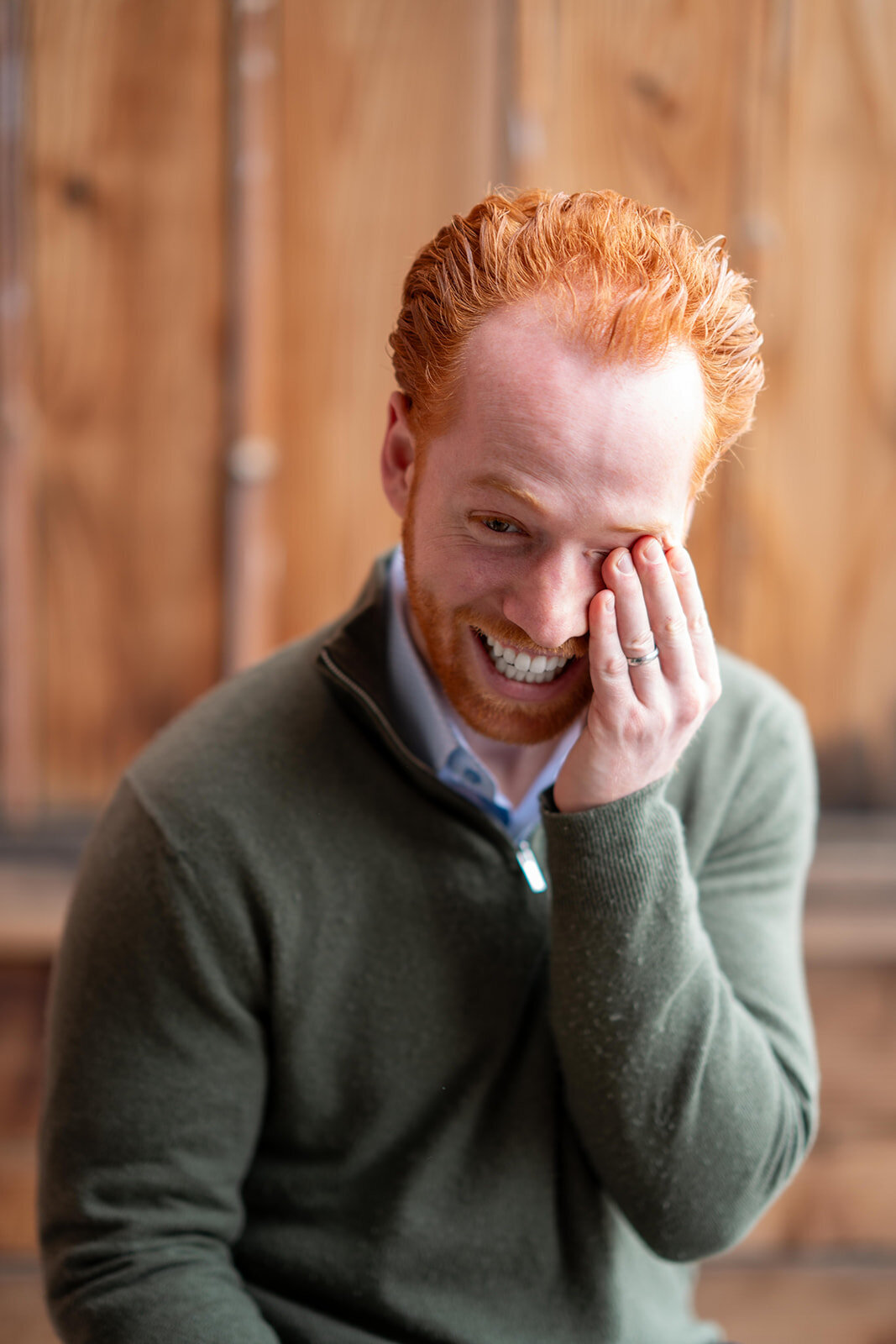 Bearded man wearing a sweater in an office laughing while holding his face