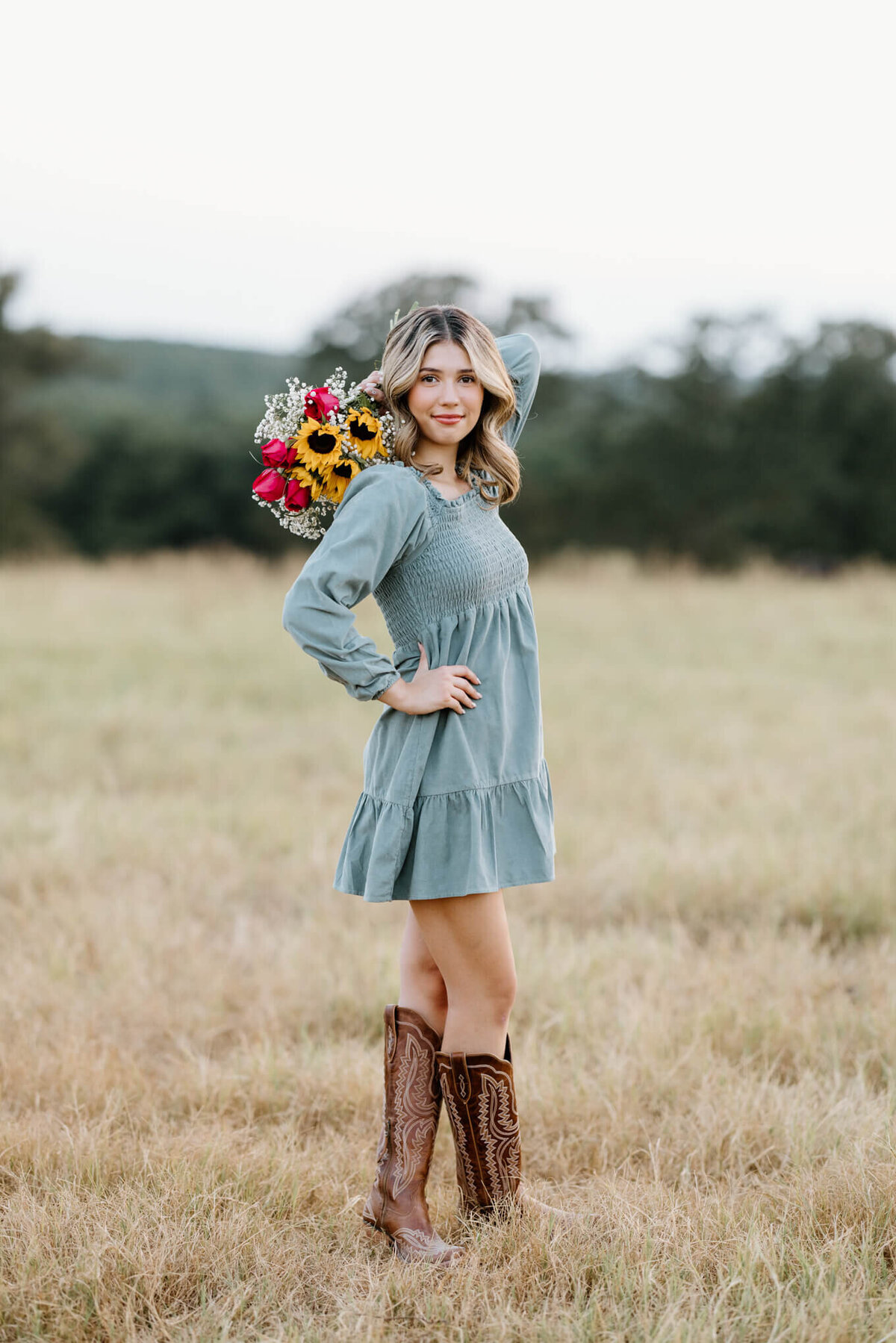 senior girl in teal dress and cowgirl boots holding bouquet of  flowers in hand