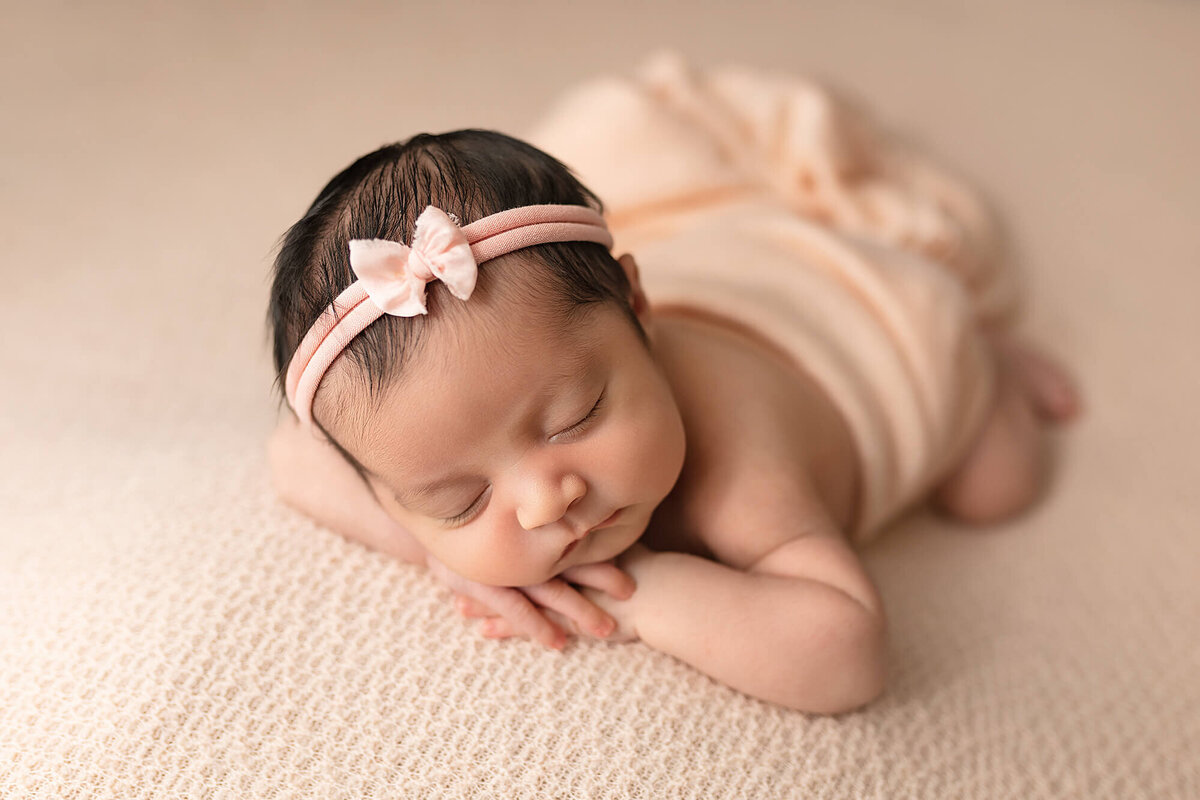 Baby girl posed on pink with pink bow.