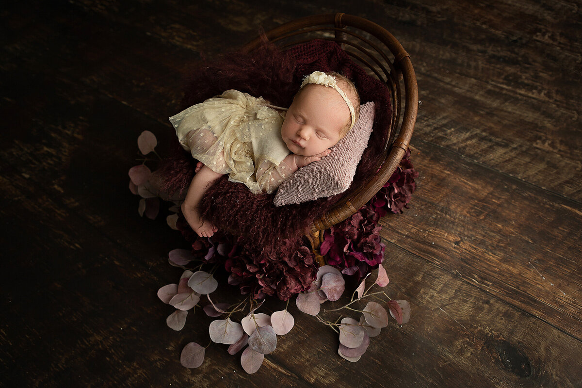 newborn-photographer-near-me-in-columbus-ohio-sleeping-baby-girl-on-tiny-papasan-chair-with-purple-accents