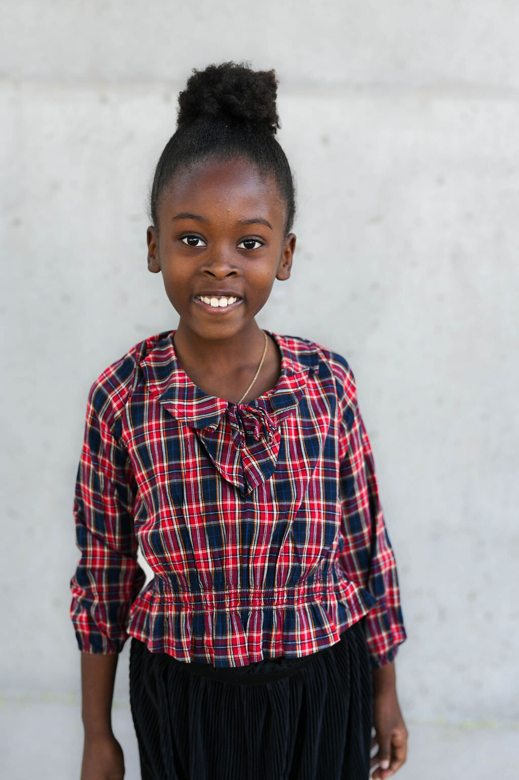 A child smiling while standing against a plain wall.