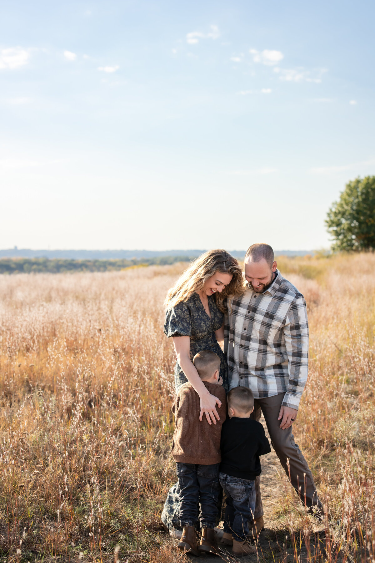 a family with 2 young kids hug eachother while standing in a field in Cottage Grove, MN for family photos