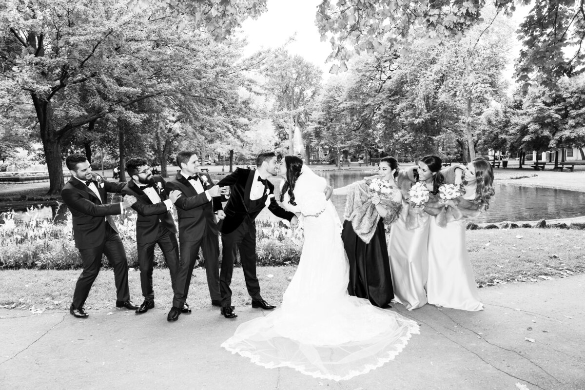 The bride and groom share a playful kiss while the bridal party humorously pulls them apart. The fun and lively scene captures the joyful and spirited atmosphere of the wedding celebration. The bridal party's antics add a touch of humor and camaraderie to the moment, making it a memorable and lighthearted part of the day.