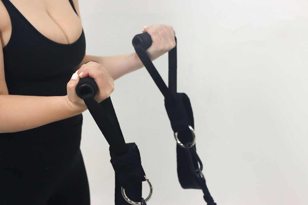 Close-up of a client performing upper body Lagree workout using Megaformer straps at Rise Lagree Studio in Poway, CA
