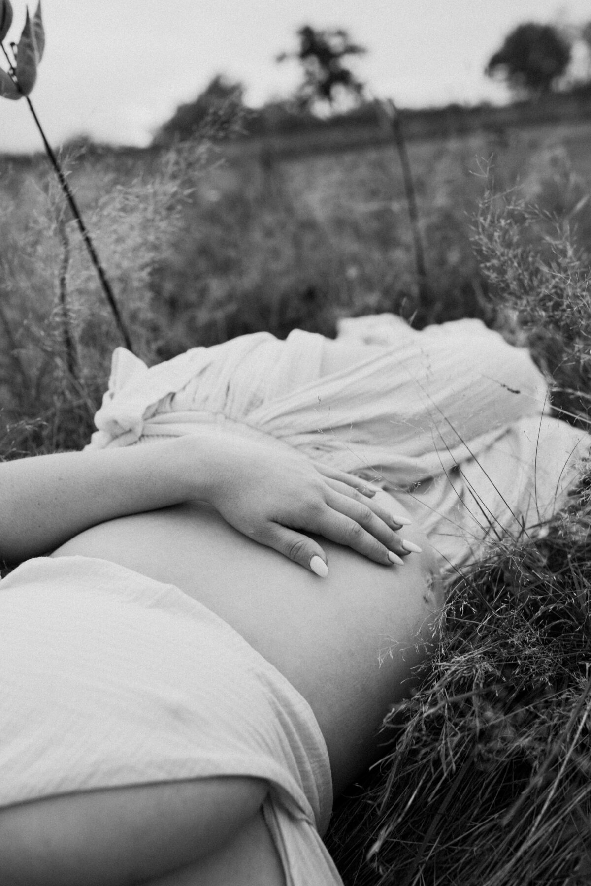 Expecting mother lying in a field with her hands resting on her belly during a peaceful maternity session in Northern Virginia